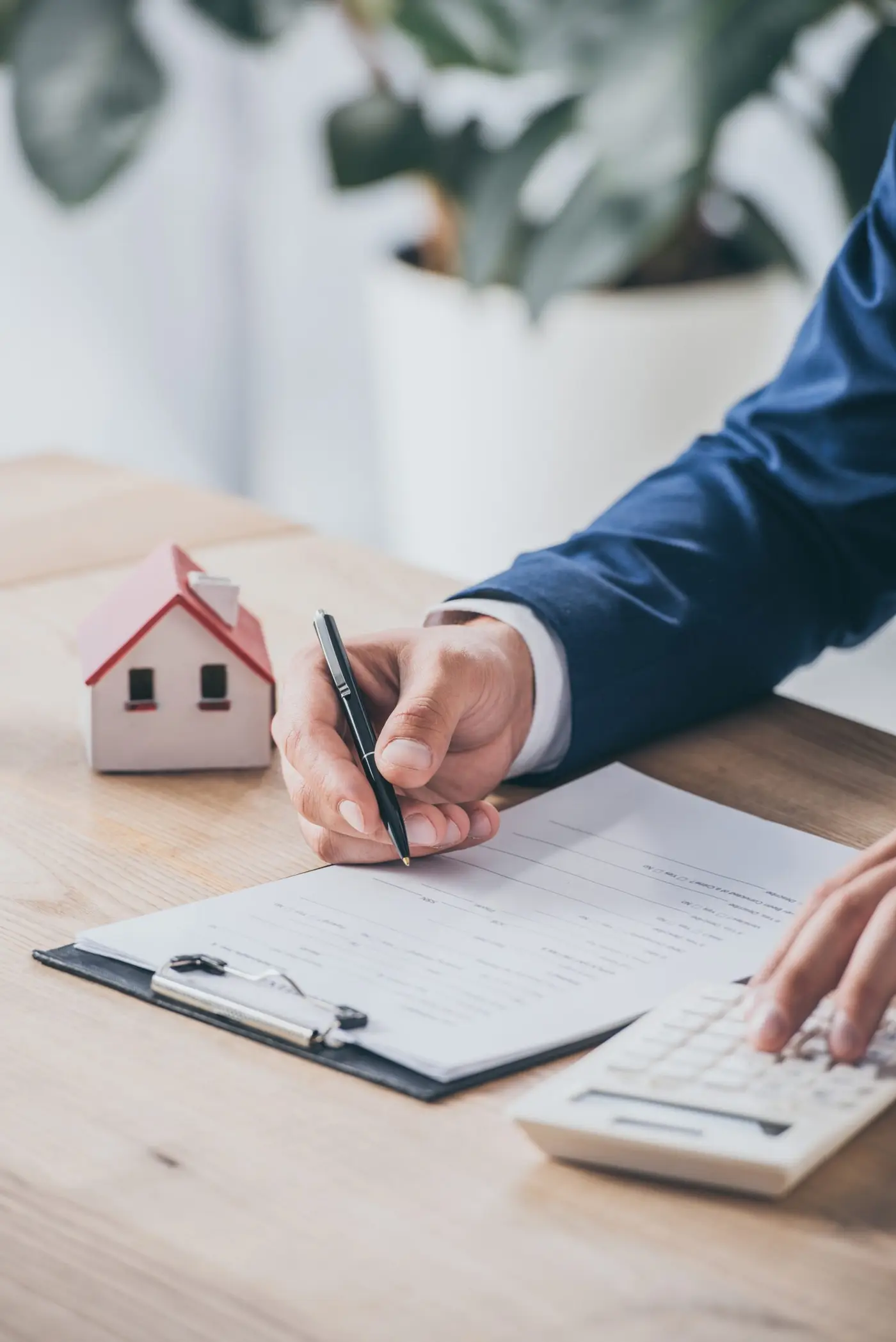 Person signing real estate documents with small house model on desk